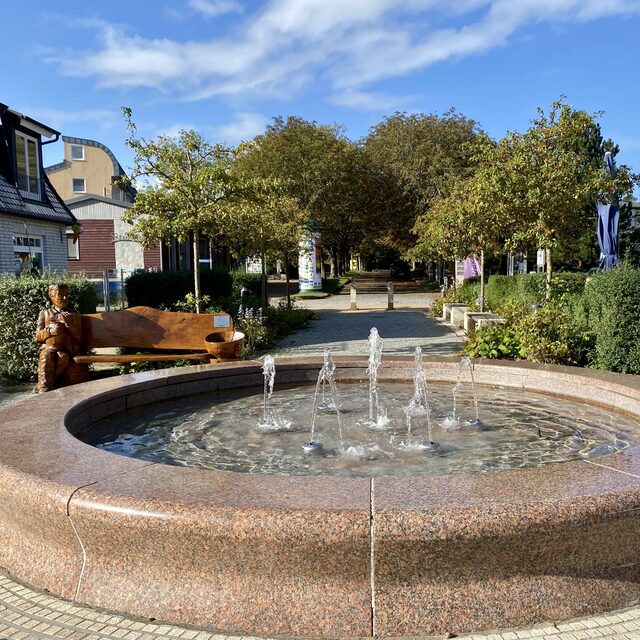 Brunnen und Promenade im Ortskern von Juliusruh an einem sonnigen Tag.