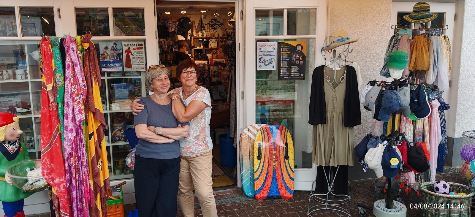Zwei Frauen umarmen sich vor dem bunt geschmückten Eingang der Strandgut Buchhandlung in Juliusruh.